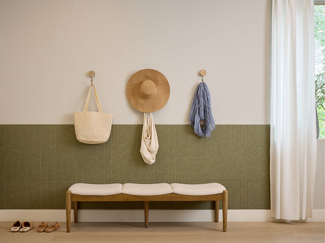 Entryway with a bench, hat, bag, and shoes against a wall with a Felt Right wall design in green textured panel.