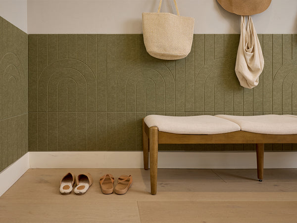 Square tile with engraved arch pattern in sage green, displayed on floor in entryway setting with wooden bench and accessorie