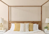 Cream-colored tile wall with engraved curved geometric line pattern behind wooden bed headboard.
