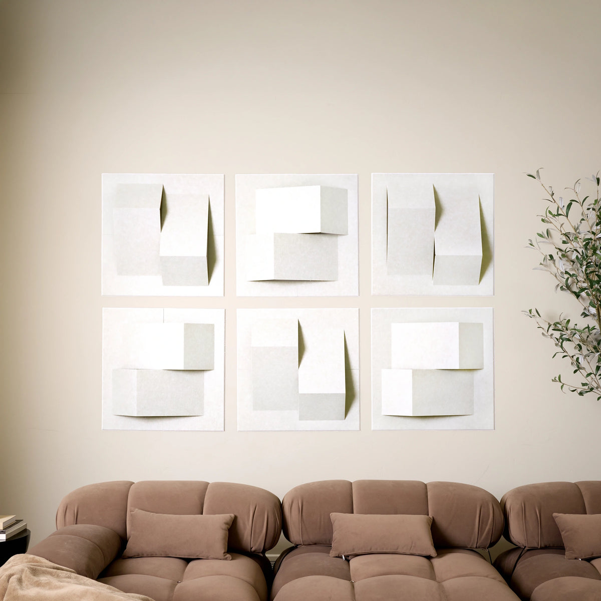 Six white acoustic felt wall tiles arranged in a 3D peak design as art above a sofa