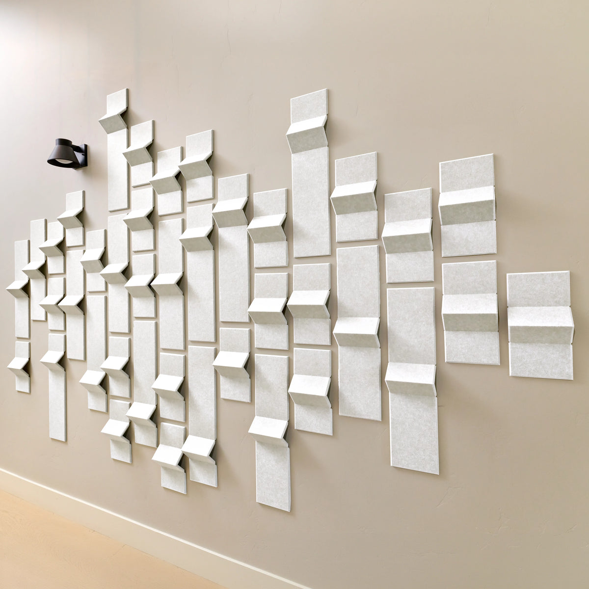 White acoustic felt tiles with peaks of dimension along a hallway wall with a light