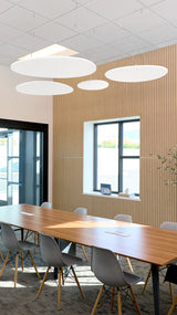 Four white flat circular acoustic baffles suspended from ceiling in modern office conference room.