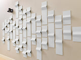 White three-dimensional tiles arranged in a gradient pattern on a beige wall with a black sphere for scale reference.