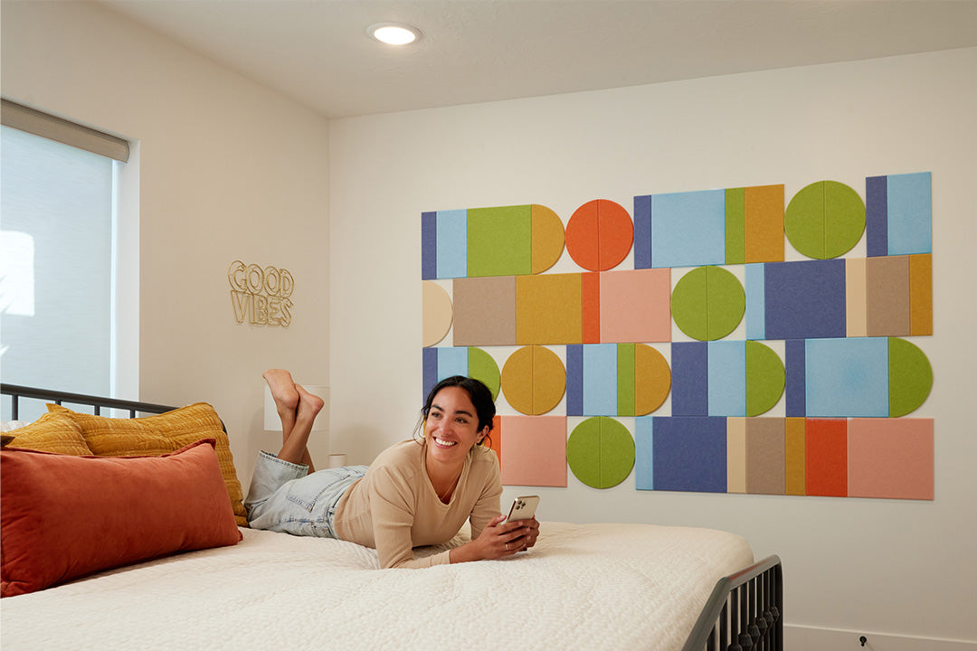 Woman lying on a bed in a room with colorful wall art and 'Good Vibes' sign.