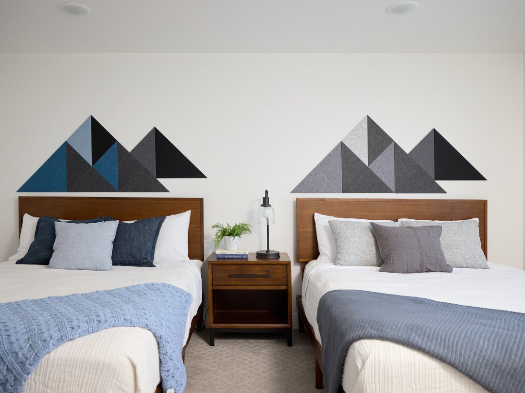 Two beds with wooden headboards and geometric felt mountain wall art in a bedroom setting.