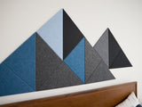 Geometric wall panels in blue and gray on a white wall above a wooden headboard.