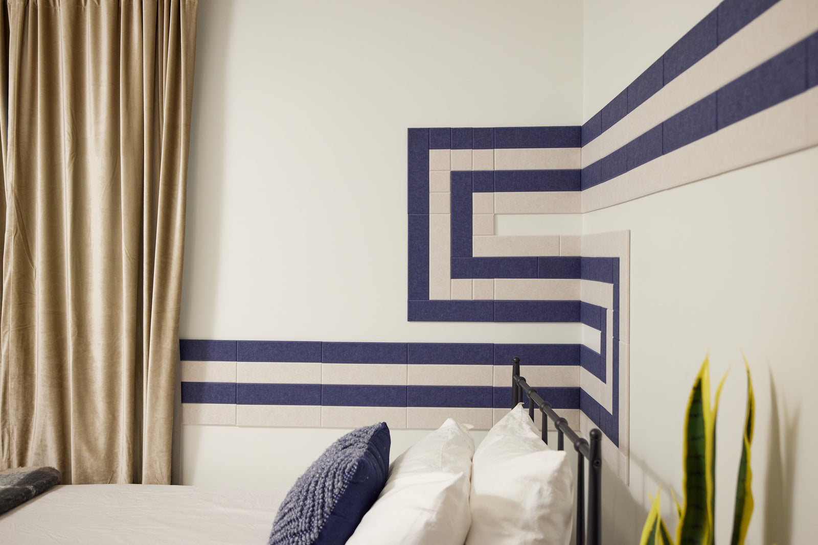 Felt Right wall art tiles in shade of blue and cream in a pipeline pattern  in a bedroom with a bed and curtains