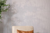 Cream upholstered chair with brown leather pillow against textured gray-white wall with wavy pattern and potted plant.