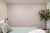 Mauve wall tiles with geometric line patterns installed in bedroom above bed with potted plant beside.