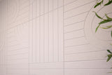 Beige ceramic tile surface with geometric line patterns and curved designs, green plant stems visible in corner.
