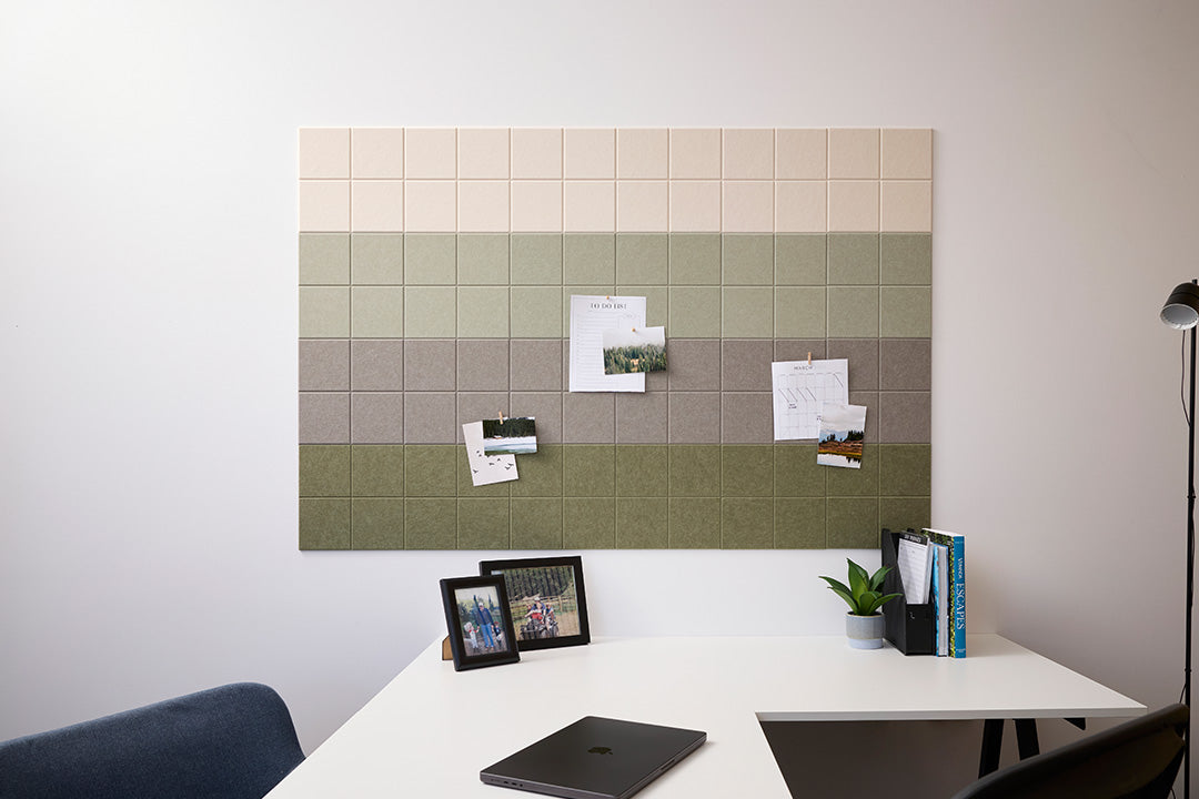 A Felt Right wall design that can work as a bulletin board with a green ombre design, mounted on a wall above a white desk. The board is decorated with notes, photos, and pins.