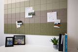 Fabric wall panel in green ombre gradient with grid pattern, displayed above desk with pinned photos and papers.