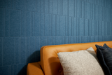 A Felt Right wall art design in a shade of blue felt tile covering a wall behind a couch.
