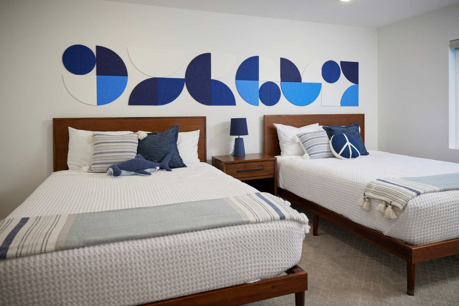 A Felt Right wall art design using circles in shades of blue and white to create a design above two beds and a night stand.