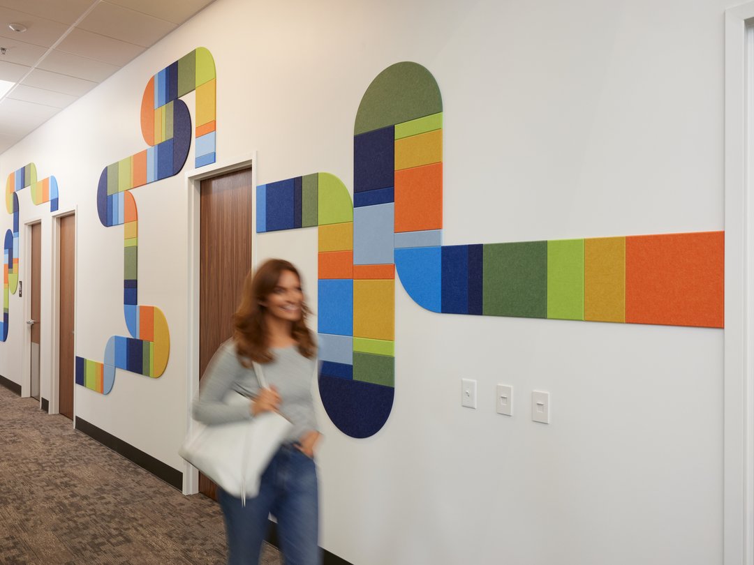 felt right wall art design in multicolors creating a pipe-like design going down a hallway with doors and a woman walking