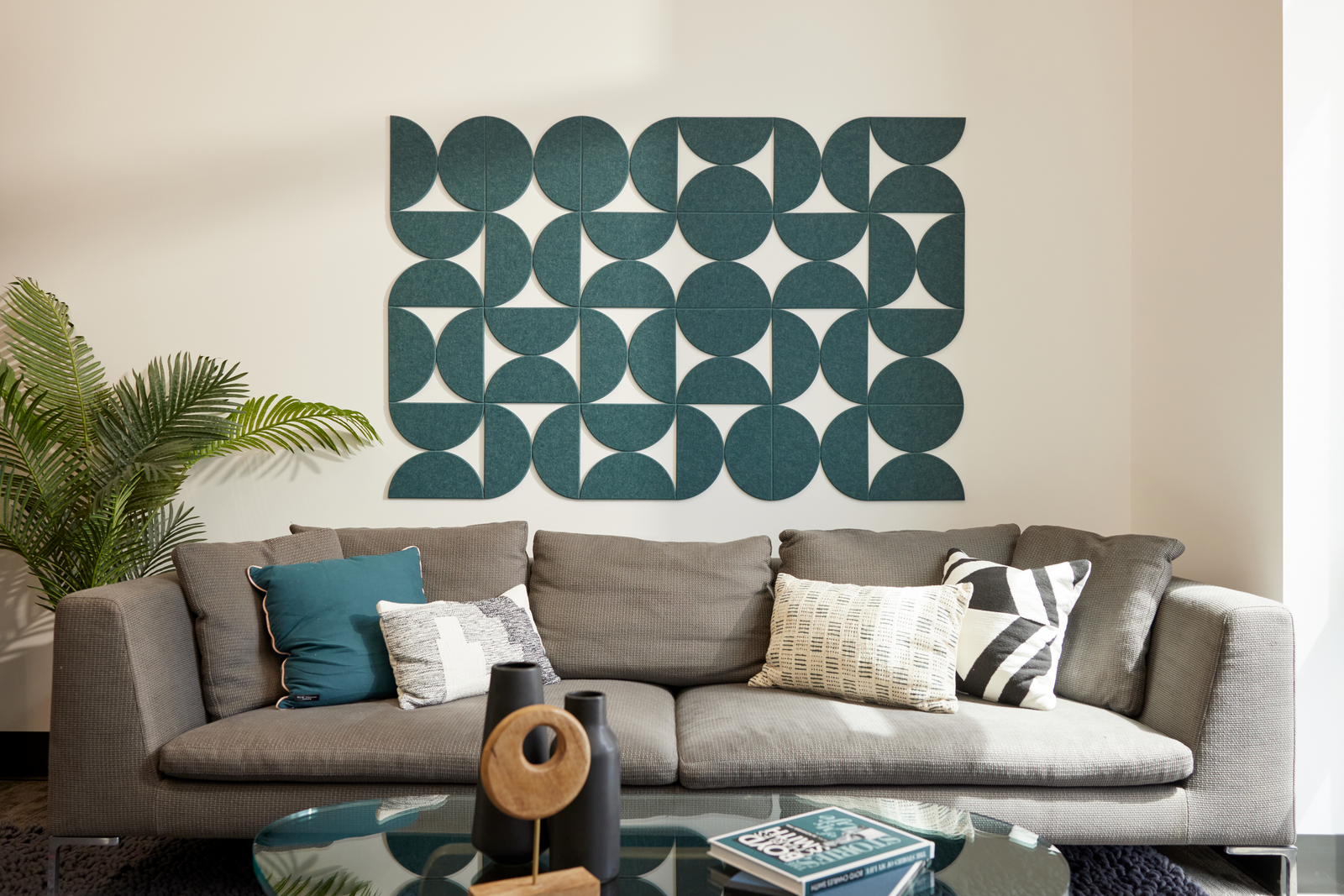 A Felt Right wall art design contemporary geometric-patterned artwork in blue green  hue with negative space, displayed above a gray sofa in a living room setting.