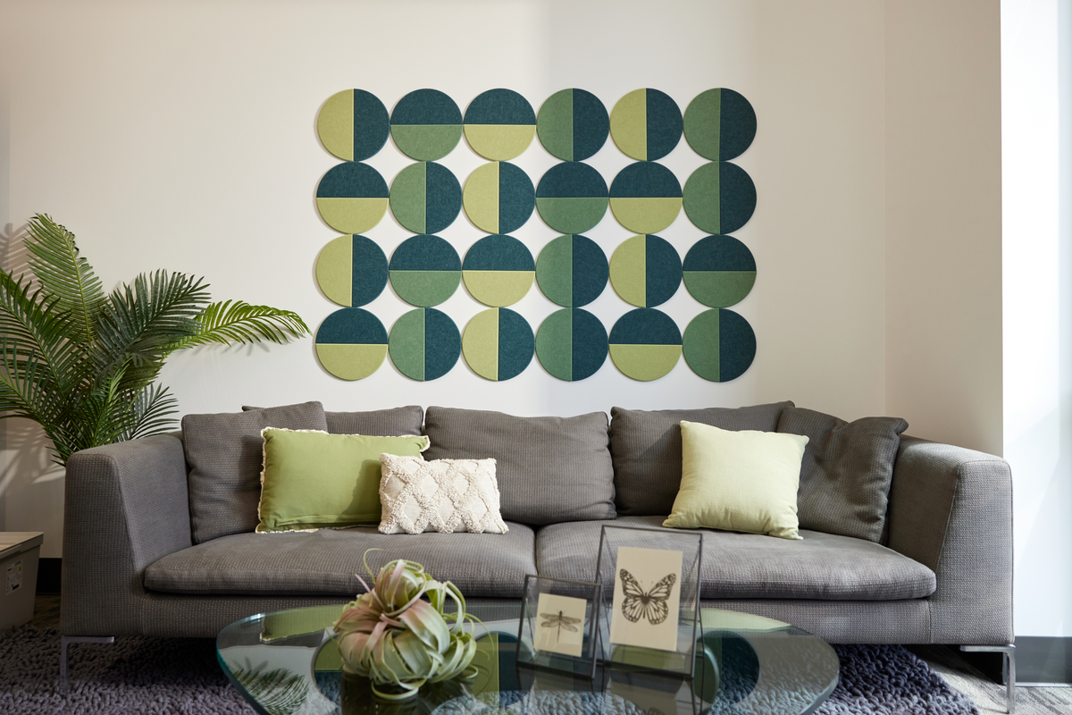 A room with a gray sofa and green decorative pillows, featuring a  Felt Right wall decal with a geometric pattern of circles in shades of green and blue.