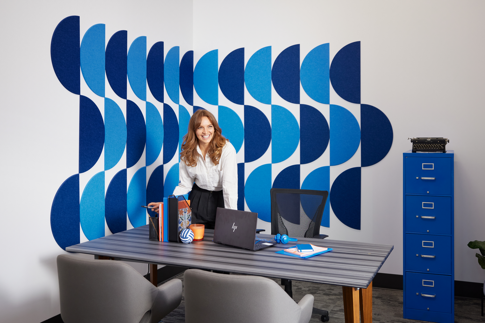 A Felt Right wall art design in shades of blue half circles on a white wall in an office and a filing cabinet.