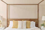 Canopy bed with wood frame and ivory headboard, styled with white and yellow patterned pillows.
