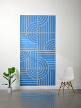 Blue felt sheet with geometric engraved pattern of curved and straight lines in tan, displayed vertically on white wall.