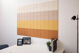 Large wall art made of square tiles in gradient colors from cream to ochre and terracotta.