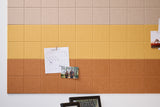 Cork board panel with ombre color gradient from beige to gold to terracotta, displaying calendar and photos.