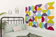 A Felt Right wall design using half circles in the shades of purple, blue, yellow, green, and cream on a wall next to a bed.
