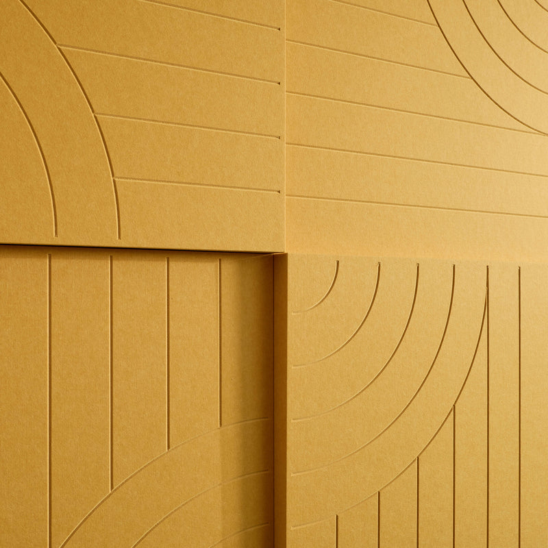 A close-up of a textured tan or ochre surface with embossed geometric arches and linear paneling, filling the entire frame.