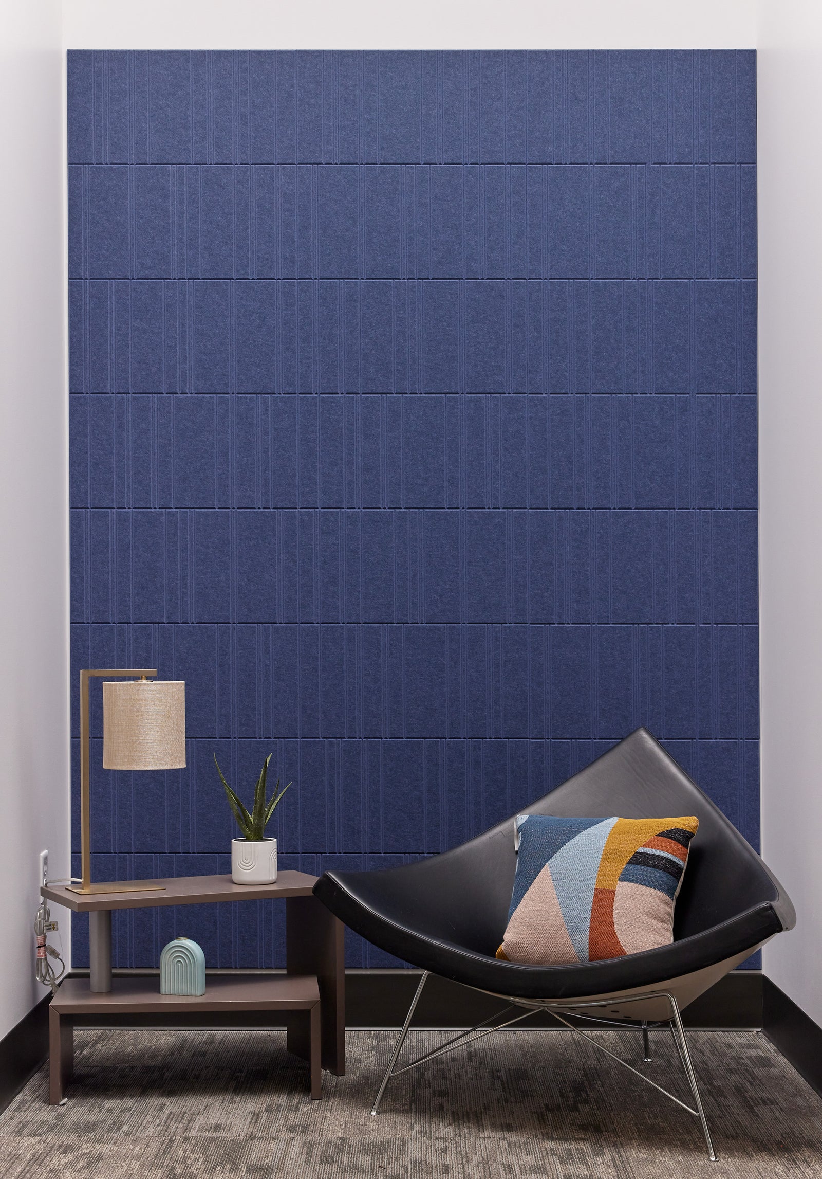 A Felt Right wall design in a shade of blue covering a wall in front of a chair and a side table.