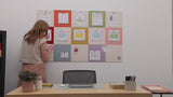 Woman pinning teacher papers onto a checkerboard rainbow bulletin board above desk.