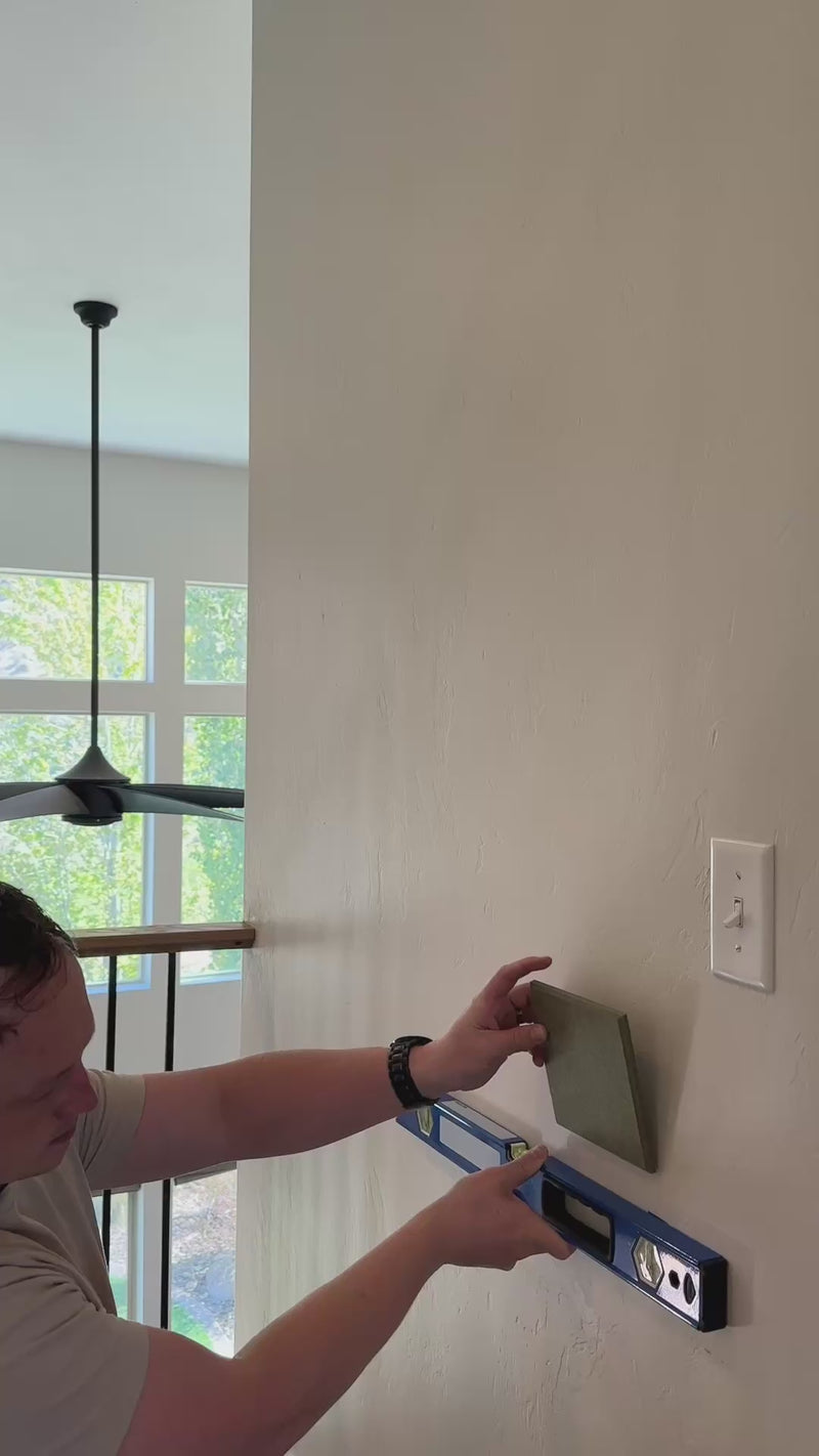 Man installing green gingham wall art using a level