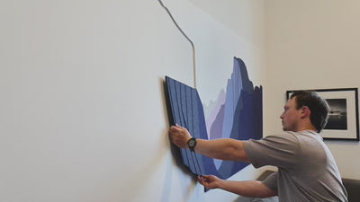 Man installing purple felt wall art above couch