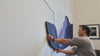Man installing purple felt wall art above couch