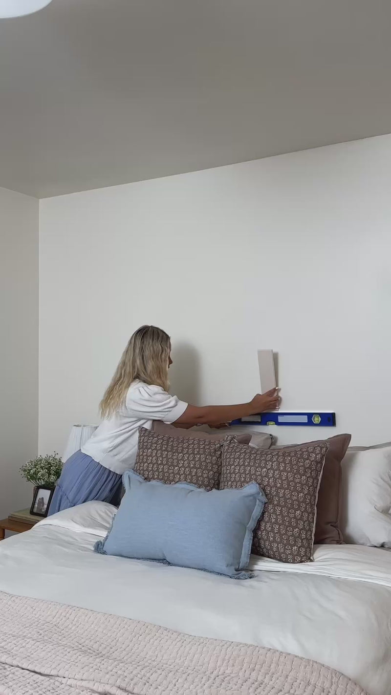 woman installing peel and stick acoustic panels above bed as a headboard.
