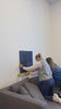 Women installing navy blue dimensional wall panels above a couch in an office.