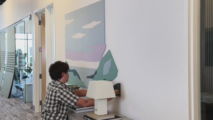 man installing coastline wall art above credenza in commercial hallway