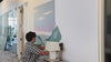 man installing coastline wall art above credenza in commercial hallway
