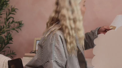 Woman putting adhesive tabs on the back of a felt pinboard and installing it on a pink wall.