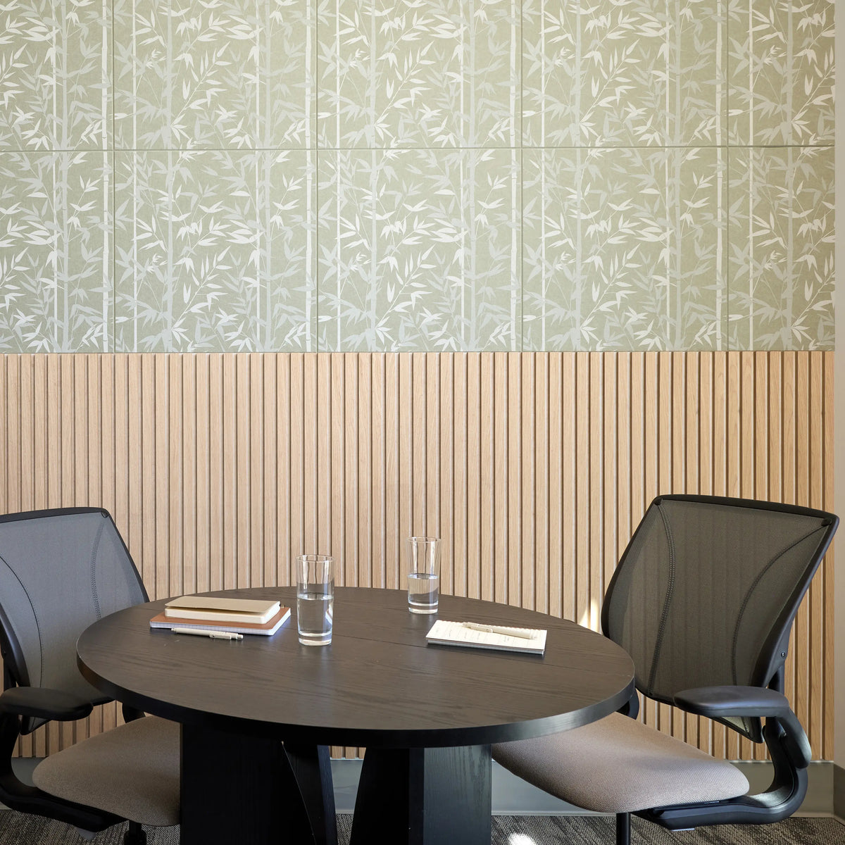 Sage bamboo print felt panels above wood slat wainscoting behind a round meeting table