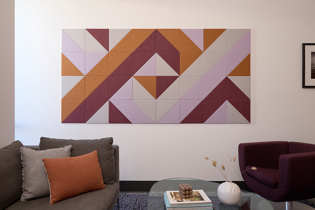 A Felt Right wall design in a geometric artwork featuring triangles in shades of orange, purple, and beige mounted on a wall in a living room setting.