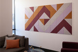 Abstract wall art with geometric triangular tiles in warm brown, burgundy, and lavender tones arranged in a diagonal pattern.