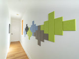A Felt Right wall art design in blue, green, and grey in a geometric pattern along a white wall in a hallway.