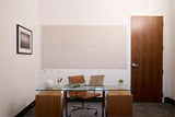 Modern office space with glass desk, wooden chair, wall art, and beige textured wall panel above workspace.