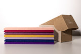 Stack of folded fabric swatches in pink, burgundy, purple, gold, lavender, navy, and violet next to kraft cardboard box.