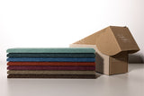 Stack of six fabric swatches in shades of teal, navy, blue, burgundy, taupe, and brown next to an open kraft cardboard box.