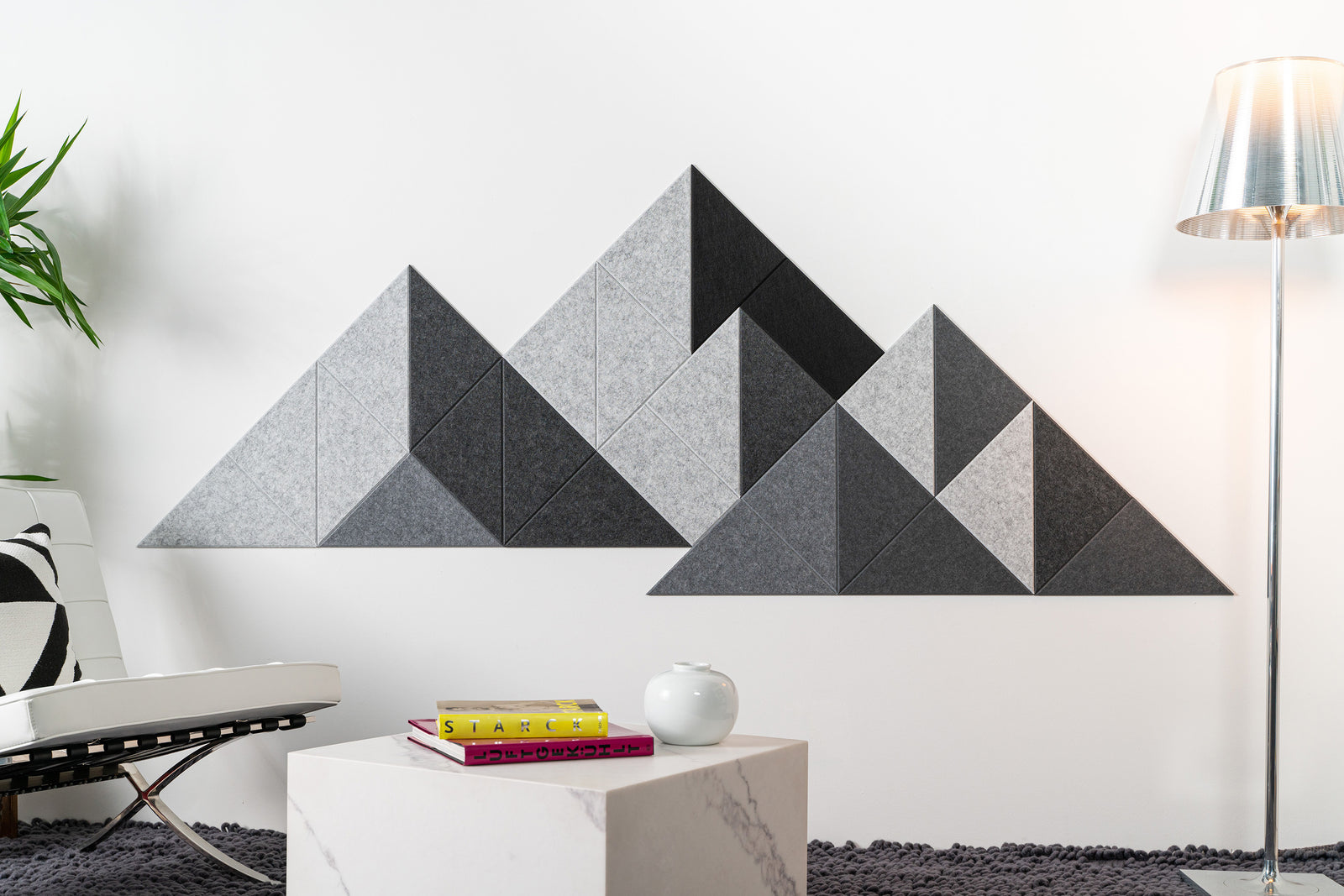 A Felt Right wall art design in shades of grey in a mountain design on a wall next to a chair and a lamp