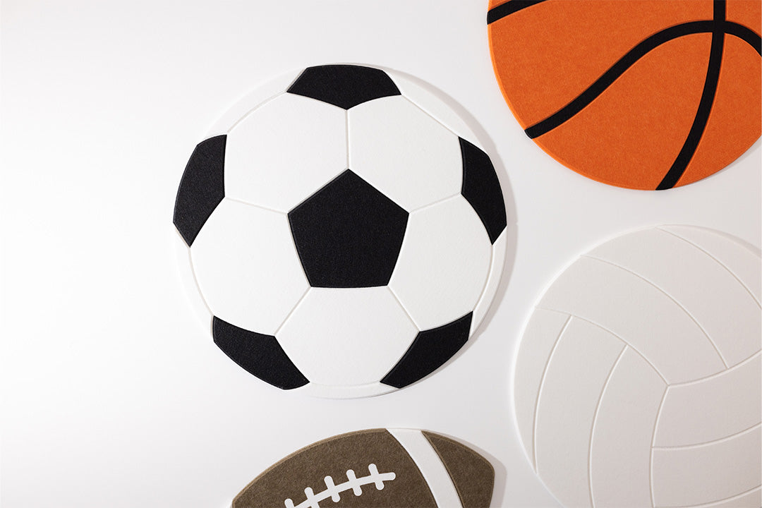A soccer ball, basketball, volleyball, and football made from noise absorbing acoustic felt wall material on a white background