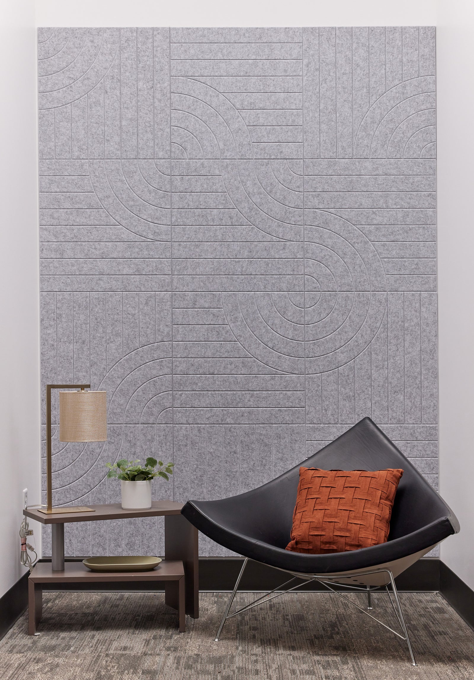 A Felt Right wall art design in shade of grey on a wall behind a chair and a side table.