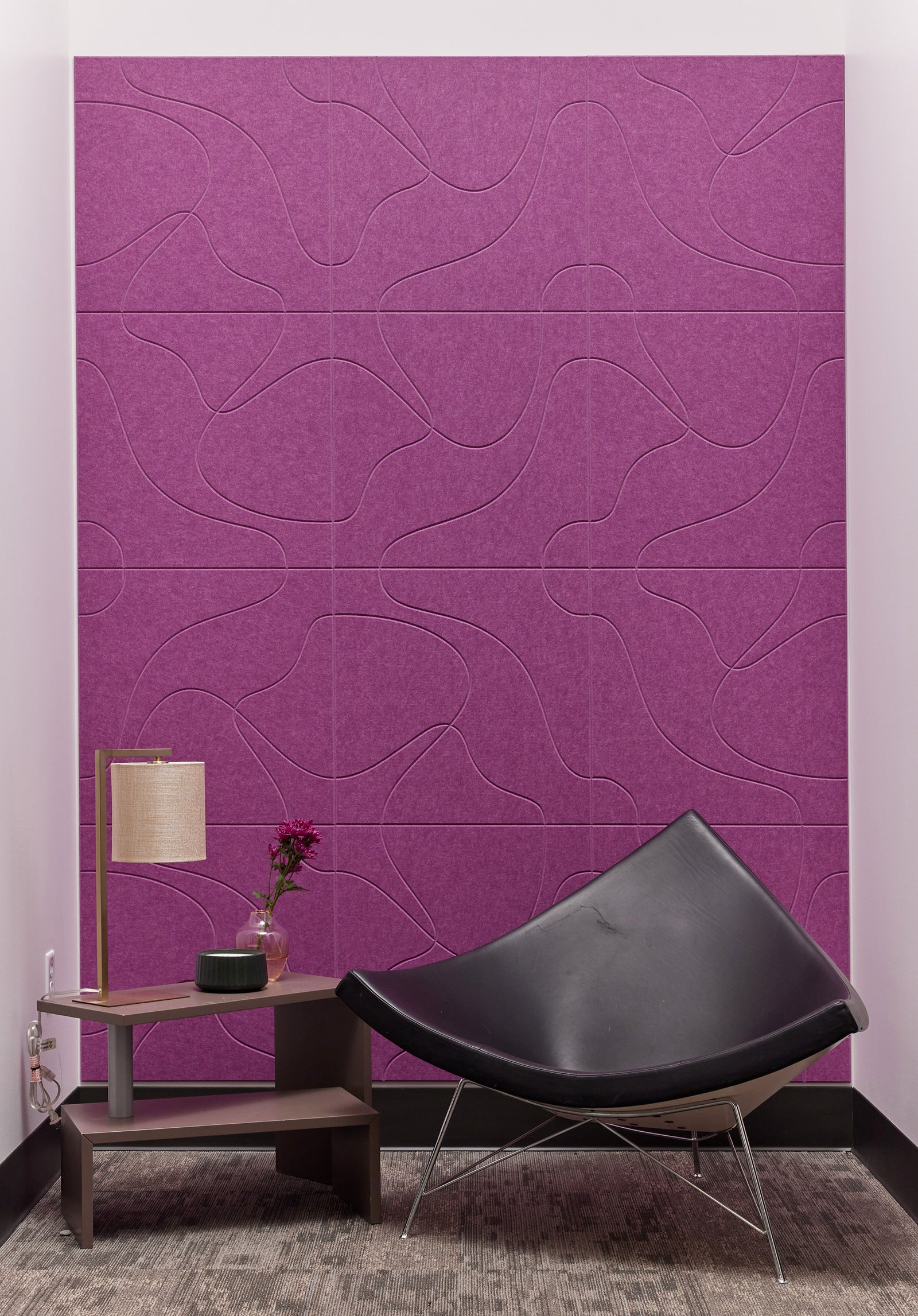 A Felt Right wall art design using a topical graphic look in shade of purple on a wall behind a chair and a side table.