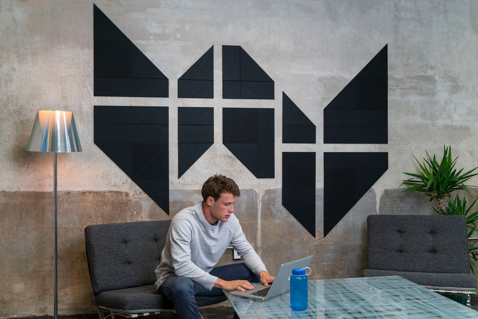 A Felt Right wall art design in black on a cement wall in a waiting room or office with two chairs and a man sitting and working on his lap top.